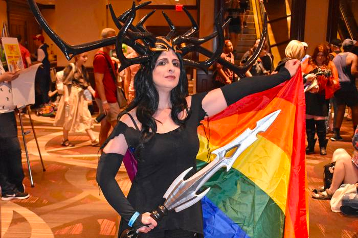 Hela cosplayer brandishing a sword, wearing a rainbow-flag cape.